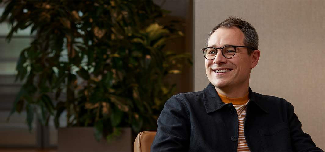 Dan sonríe, sentado en un sillón y mirando a alguien a su derecha.