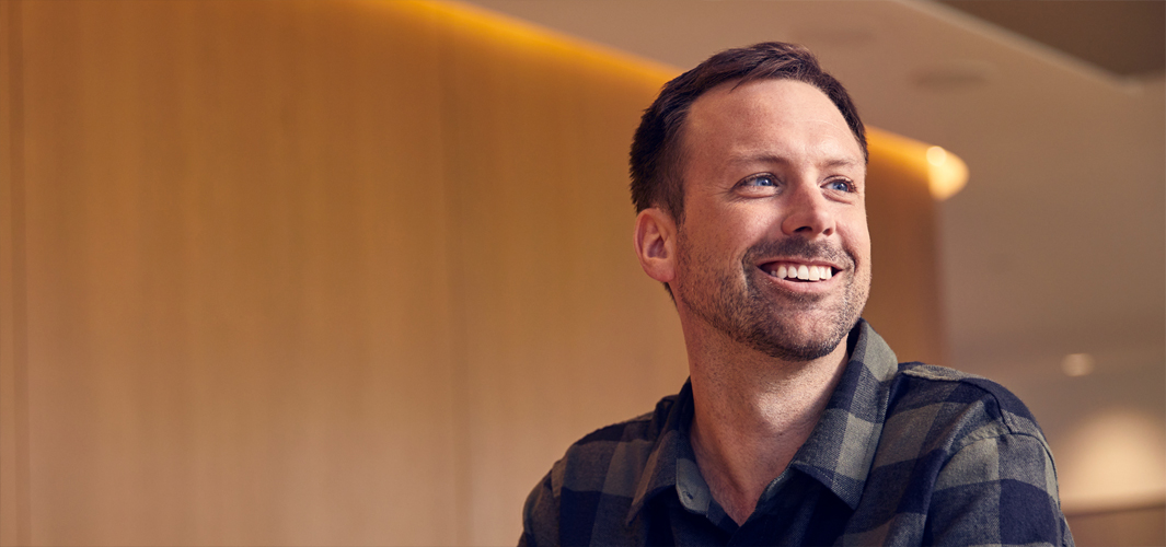 Jordan sentado sonríe con las manos entrelazadas frente a él.