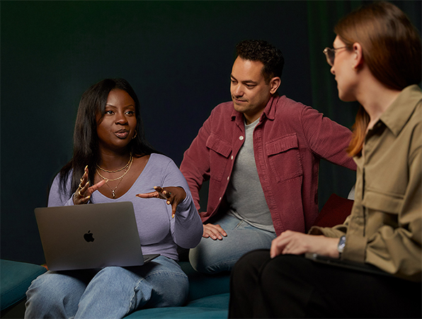 Tres personas del equipo de Servicios y Software de Apple conversan en un sillón, una de ellas con una MacBook.