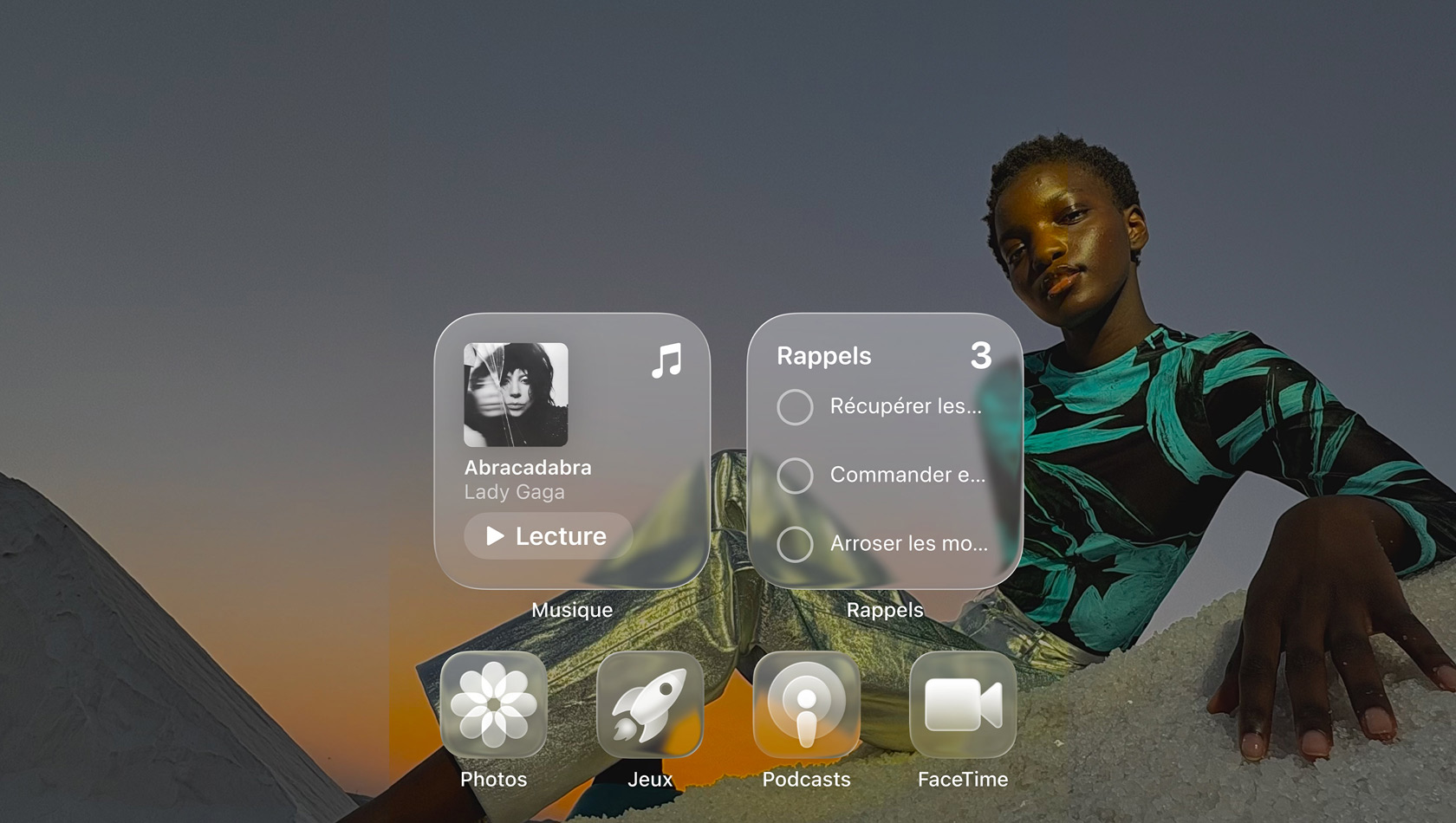 Écran en Liquid Glass avec des icônes d’app transparentes, comme Apple Music, Rappels, Photos, Jeux, Podcasts et FaceTime qui se réfractent contre le fond d’écran
