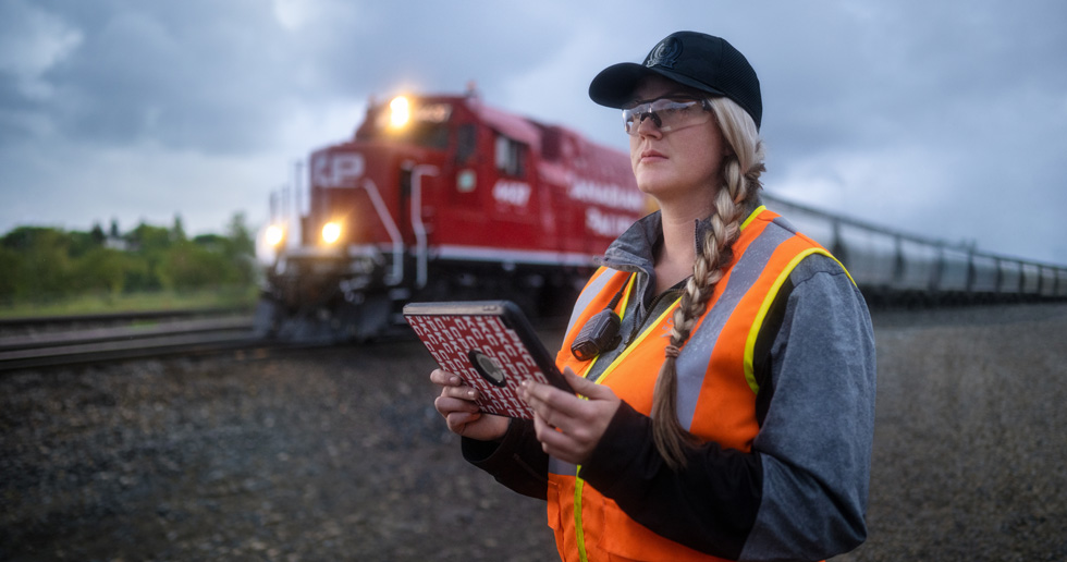 A railroad worker holds an iPad and looks out at the tracks as a train passes by