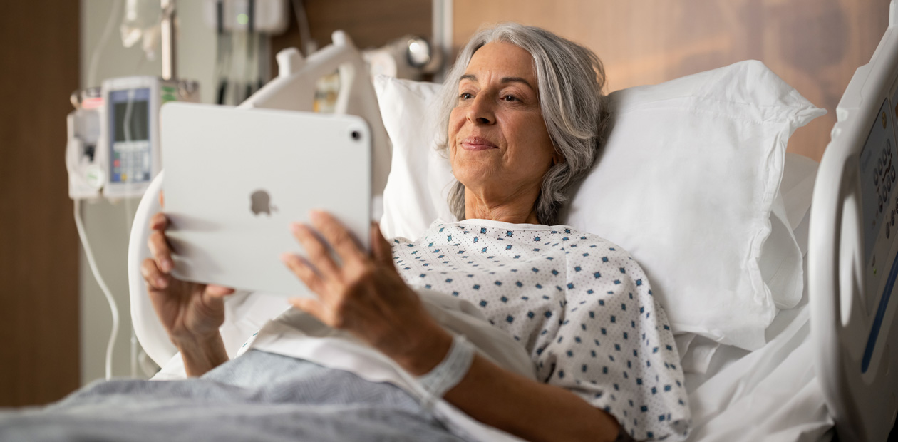 Eine Patientin liegt im Krankenhausbett und schaut auf ihr iPad.