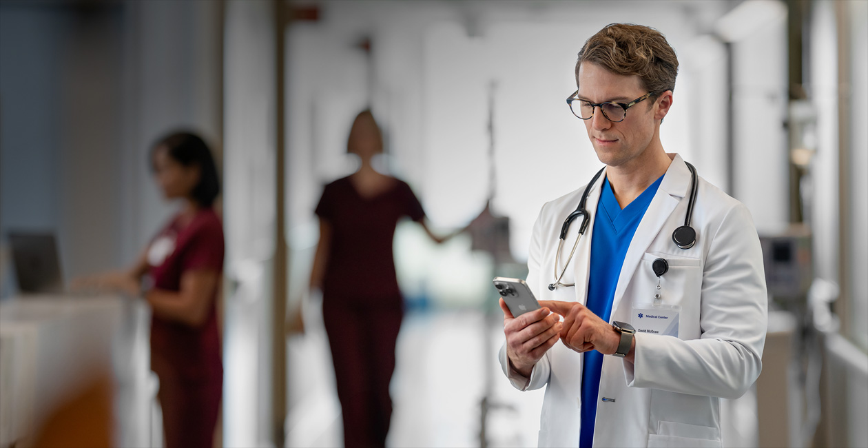 En mandlig sundhedsmedarbejder kigger på sin iPhone på et hospital.